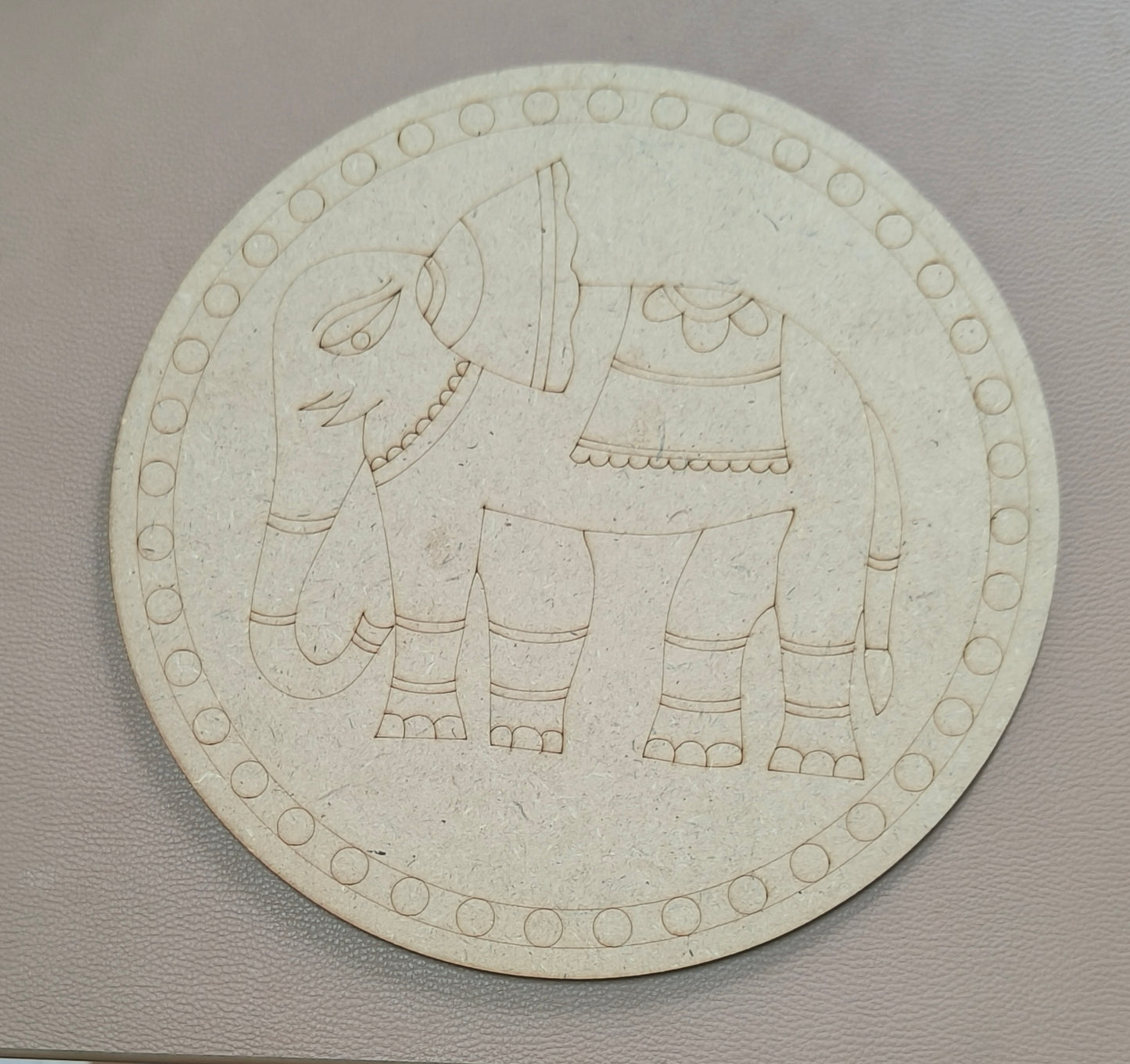 A round MDF board with elephant design on a brown background.