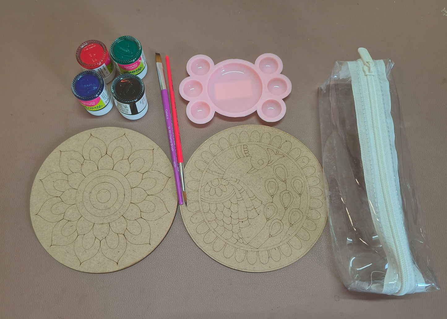 Two round MDF boards- one with peacock design and one with flower design, 4 acrylic paint bottles (red, green, blue and black), a pink palate, one purple flat brush, one red round brush, and an empty transparent pouch - all placed on a white background.