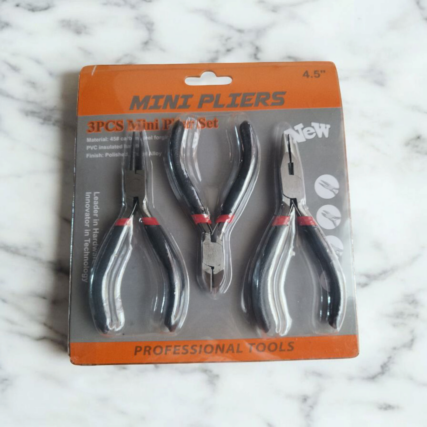 A cutter and two pliers with black handles and sharp metal blades packed together in a transparent plastic pack and placed on a marble table.