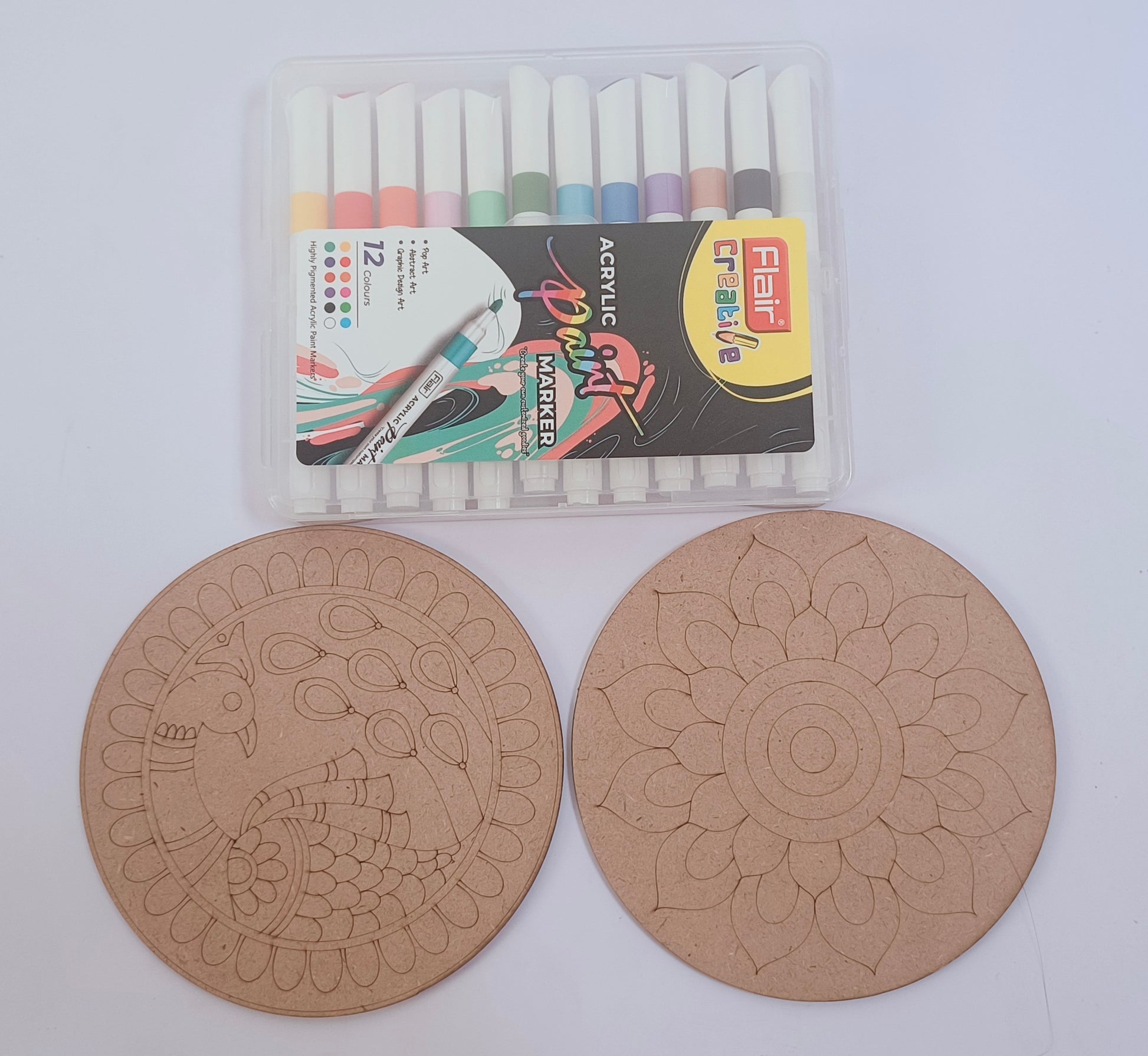 Two round MDF boards, one with peacock design and one with flower design, and a Flair acrylic paint marker set of 12 colors placed on a white background