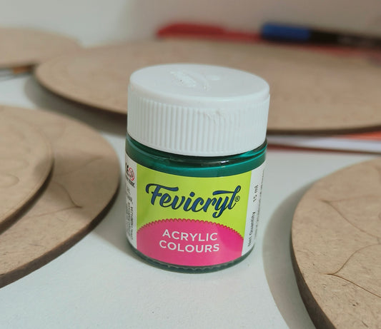 A 15ml fevicryl acrylic bottle with green paint placed on a table with mdf cutouts scattered on the table.