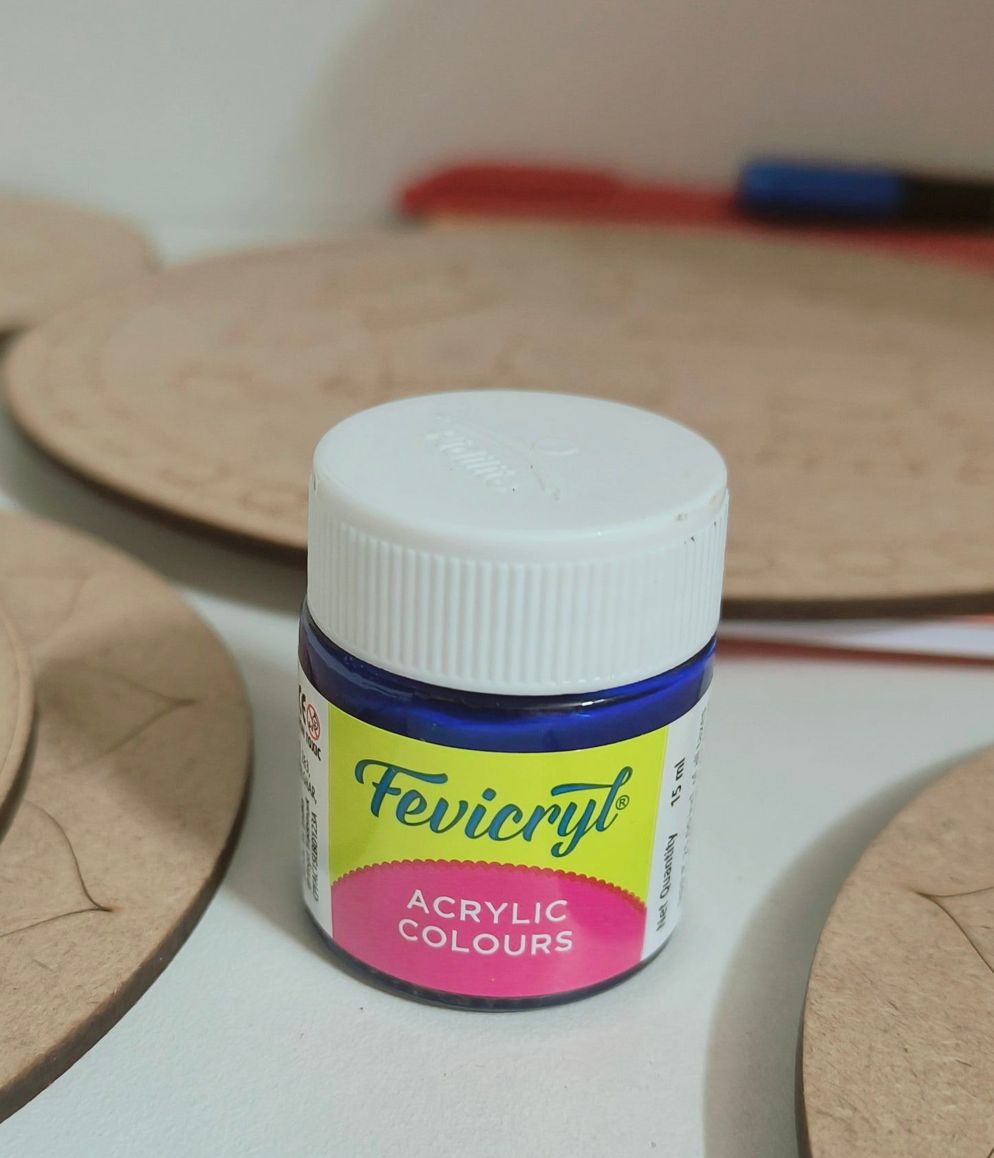 A 15ml fevicryl acrylic bottle with blue paint placed on a table with mdf cutouts scattered on the table.