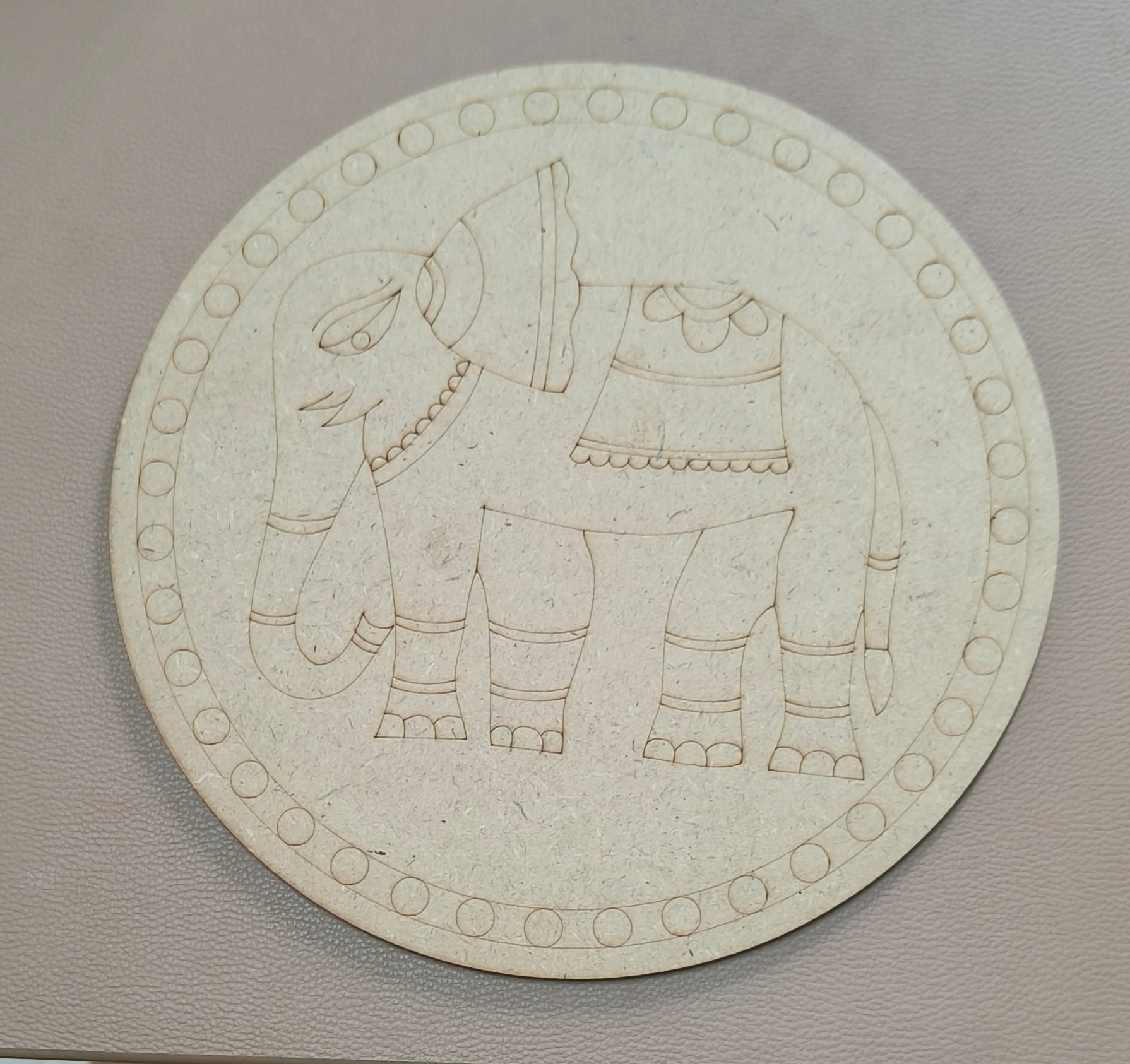 A round MDF board with elephant design on a brown background.