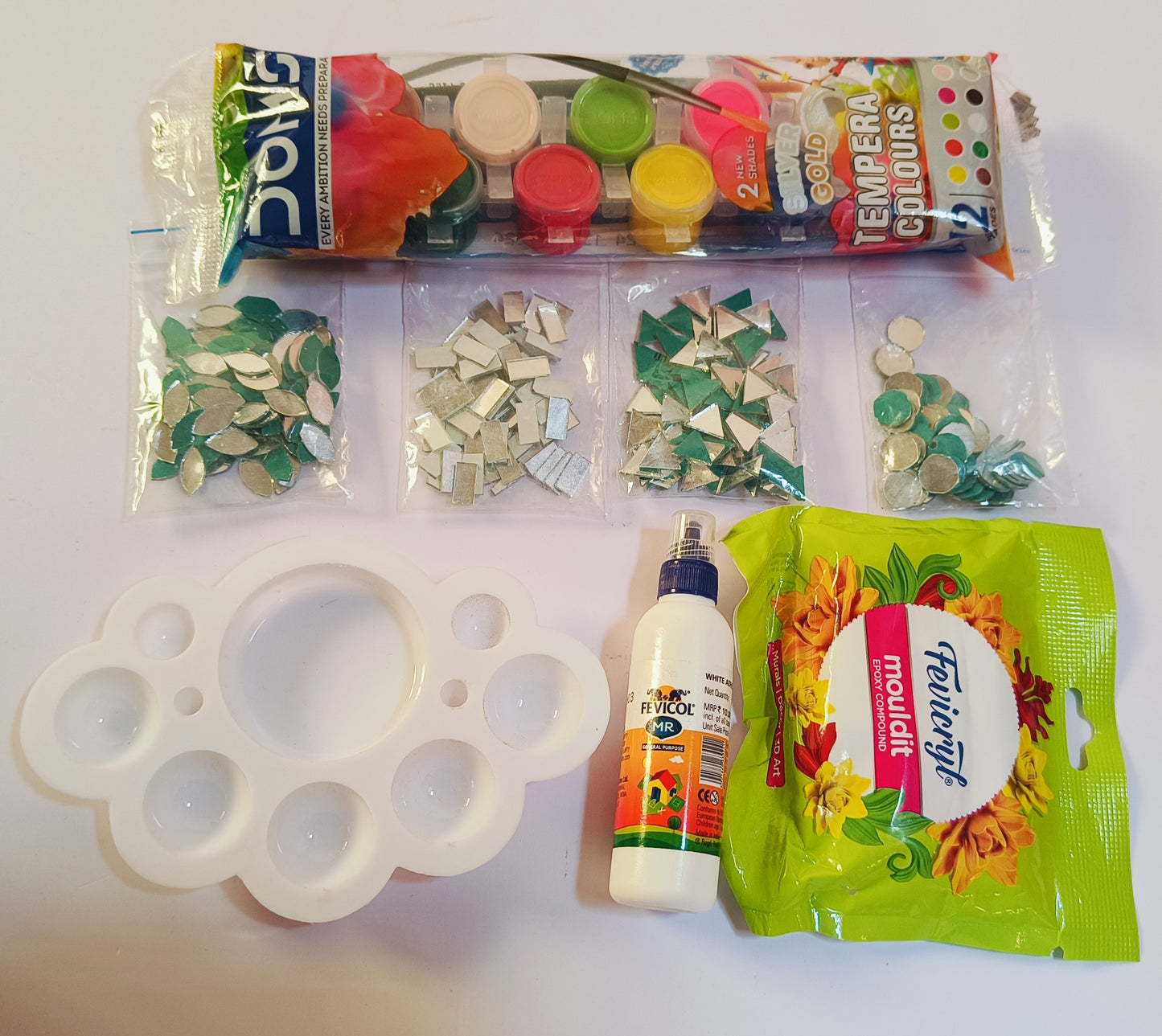 4 packets for mirrors in assorted shapes, a white palate, DOMS tempera colors packet, a fevicryl mouldit packet and a fevicol bottle - all placed on a white background.