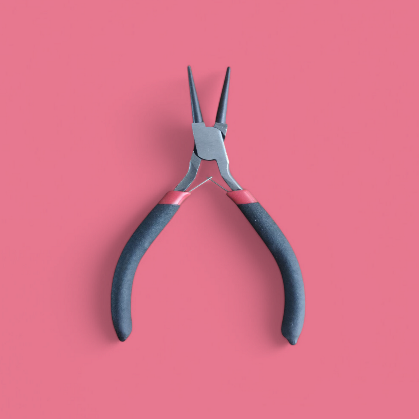 A mini plier with black handle and metal blade placed on a red background